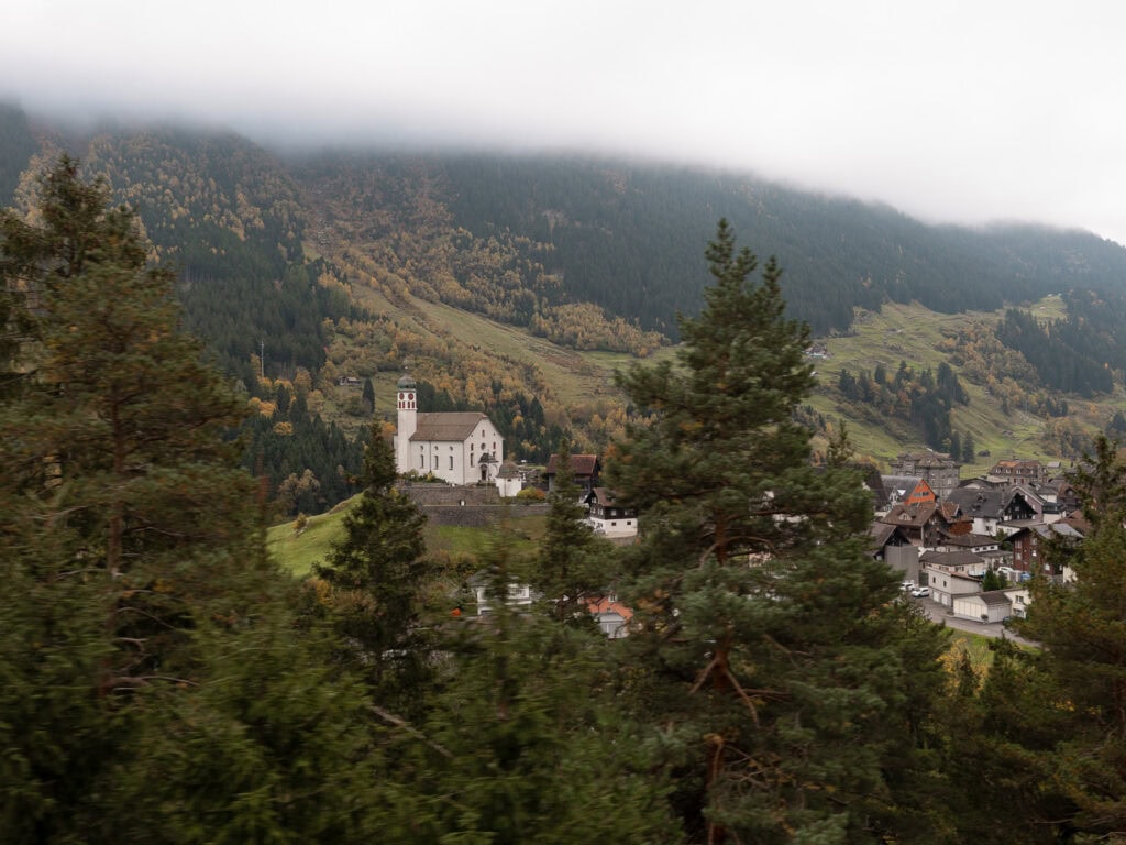 A small stone Swiss church nestled among trees and mountains along the Gotthard Railway