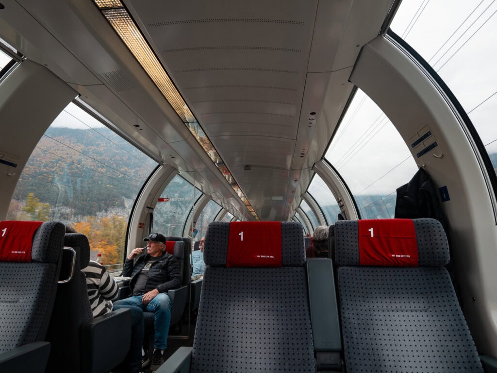 Passengers relaxing in the curved panoramic carriage of the Gotthard Panorama Express with 1st class red seats