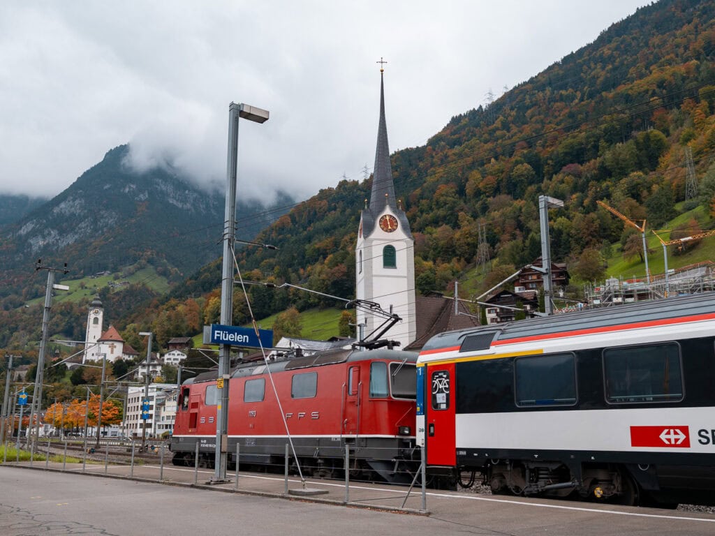 The Gotthard Panorama Express train parked at Fluelen station with a church steeple behind it