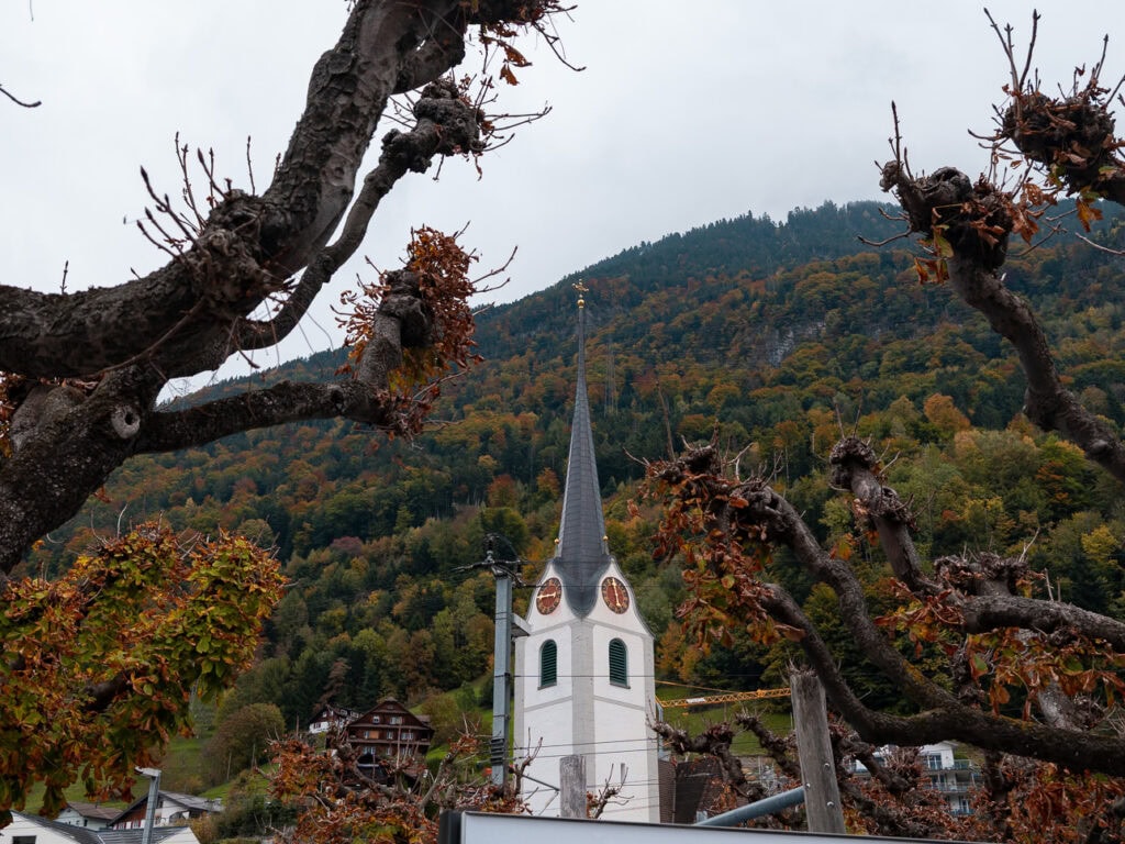 Pfarrkirche Herz Jesu church rising above Fluelen village on Lake Lucerne, framed by autumn leaves