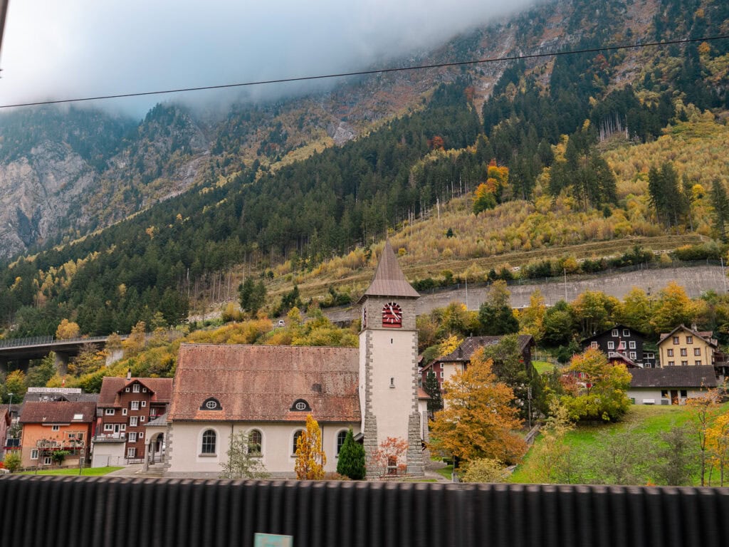 A traditional Swiss church with a stone tower seen through the window of the Gotthard Panorama Express