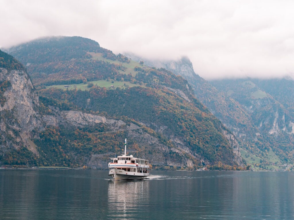 A white Lake Lucerne motor vessel cruising past misty cliffs, one of the boats used on the Gotthard Panorama Express route