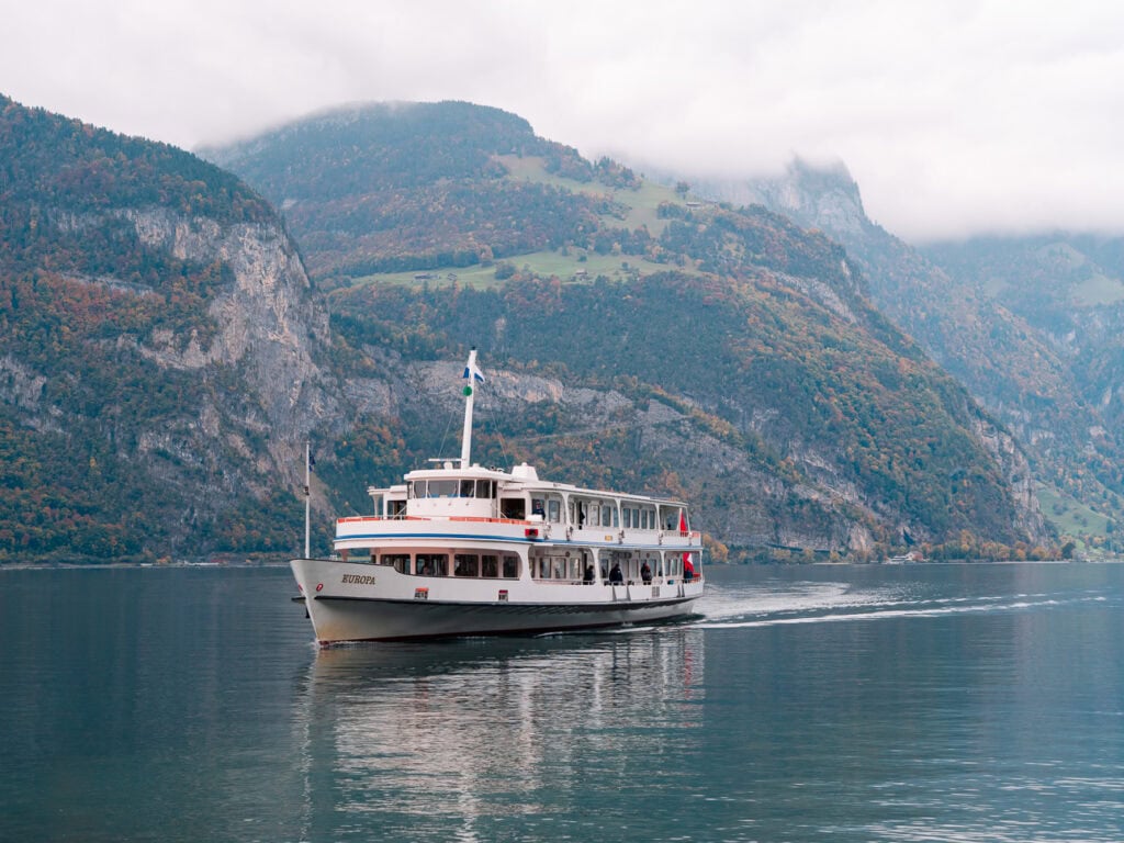 A white Lake Lucerne boat cruising past misty mountains, part of the Gotthard Panorama Express journey