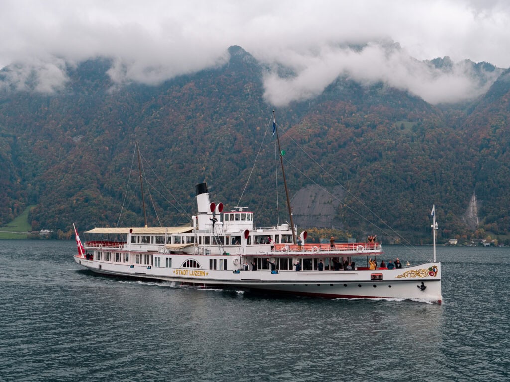A historic Lake Lucerne paddle steamer cruising past misty mountains, one of the boats used for the Gotthard Panorama Express