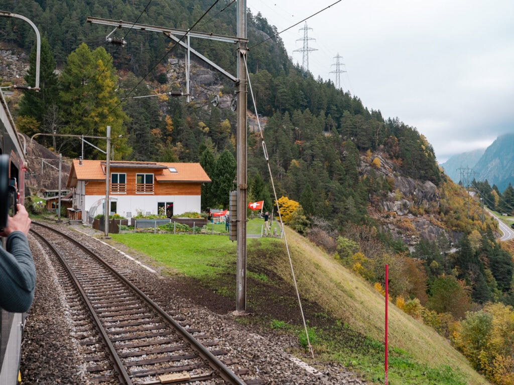 A train track running past a rural house above Wassen, where local Swiss flag wavers greet passing trains