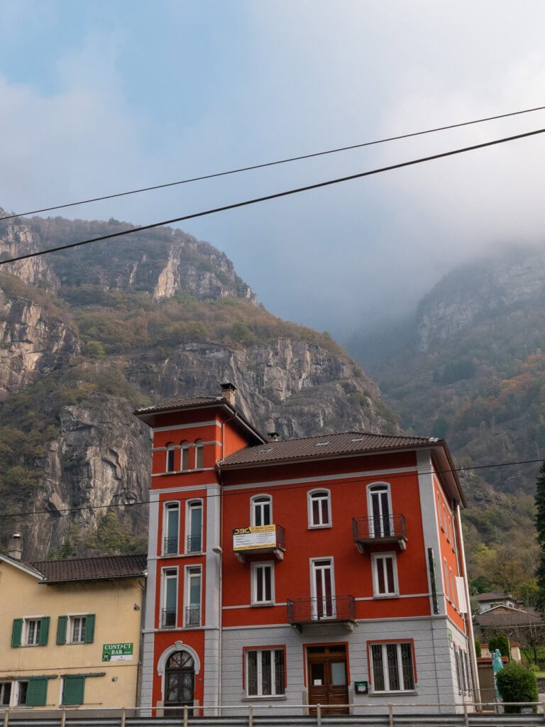 A red Swiss building with green shutters dwarfed by a massive rocky mountain behind it