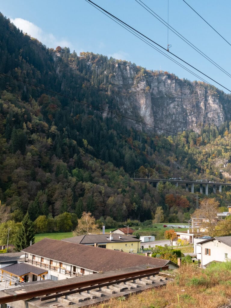 A stone viaduct curving through a steep valley with towering cliffs in the Swiss Alps