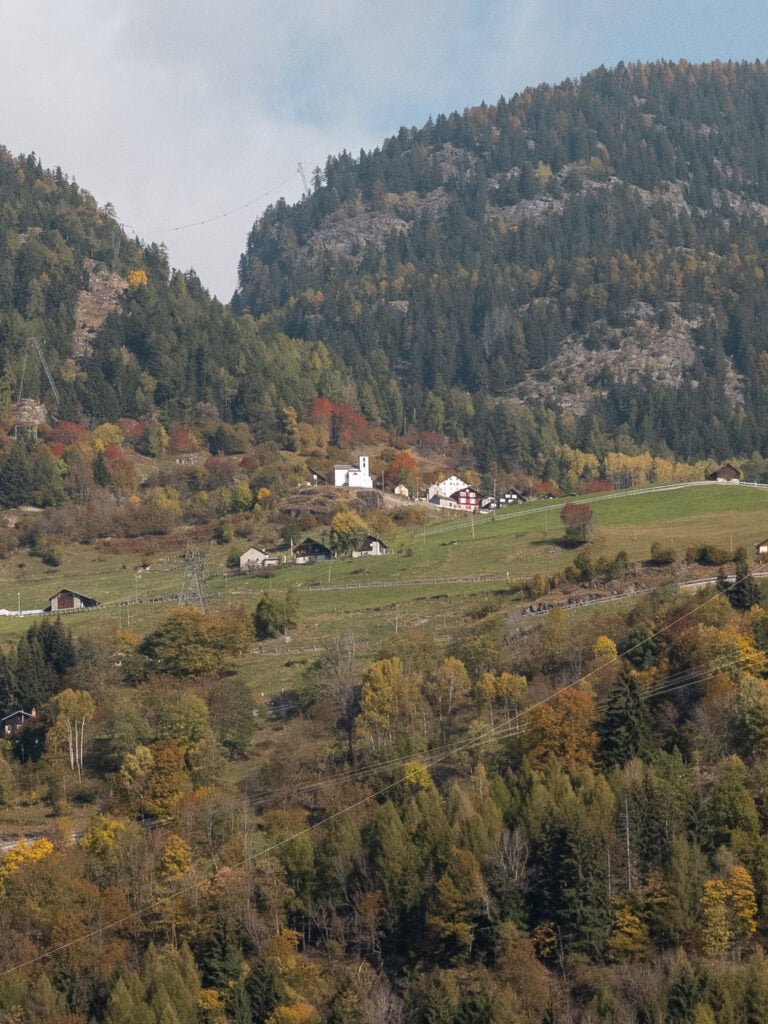 A small white church and scattered houses nestled on a green hillside in Central Switzerland