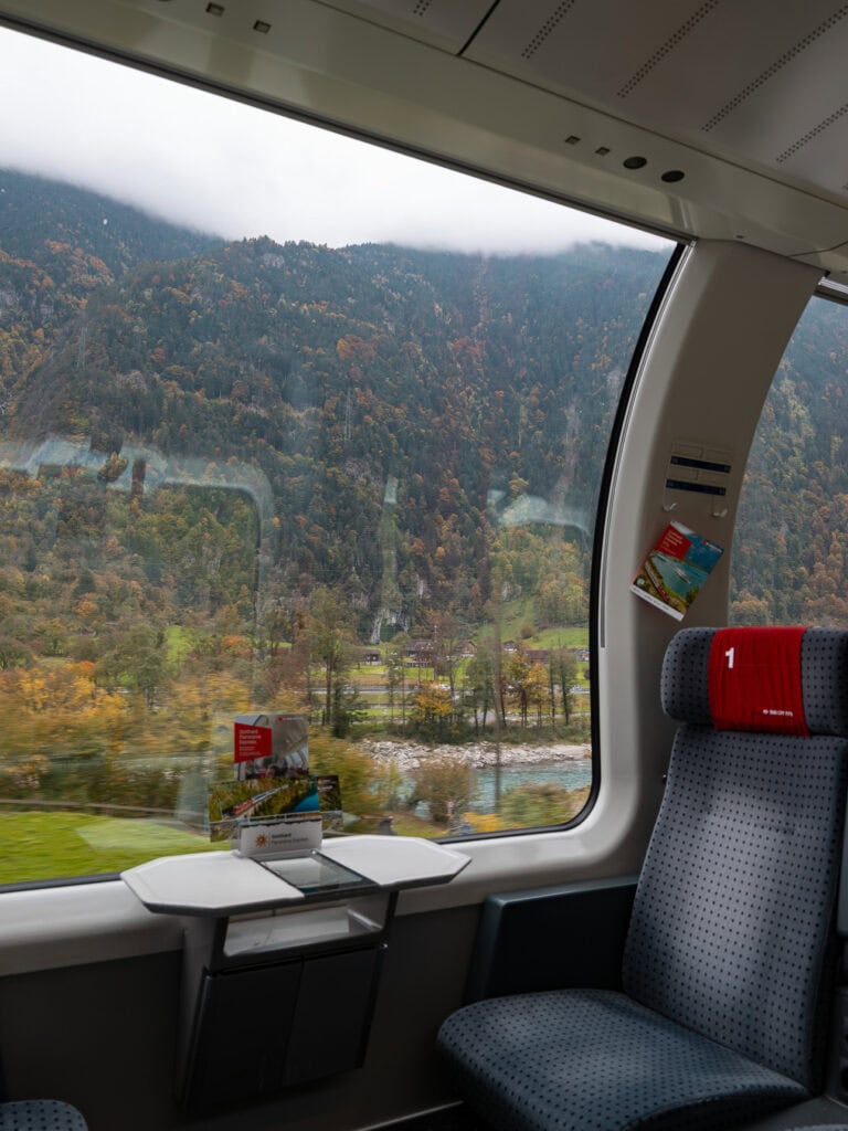 Rolling green meadows and a sliver of lake seen through the curved panoramic window of a Gotthard Panorama Express carriage
