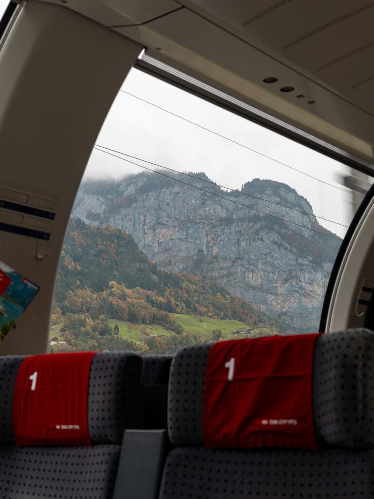 The curved panoramic window of a Gotthard Panorama Express carriage framing a Swiss mountain view