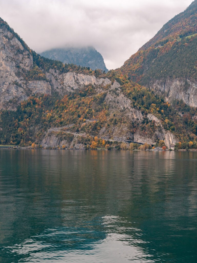 A rugged cliff face meeting the calm waters of Lake Lucerne on a misty autumn day