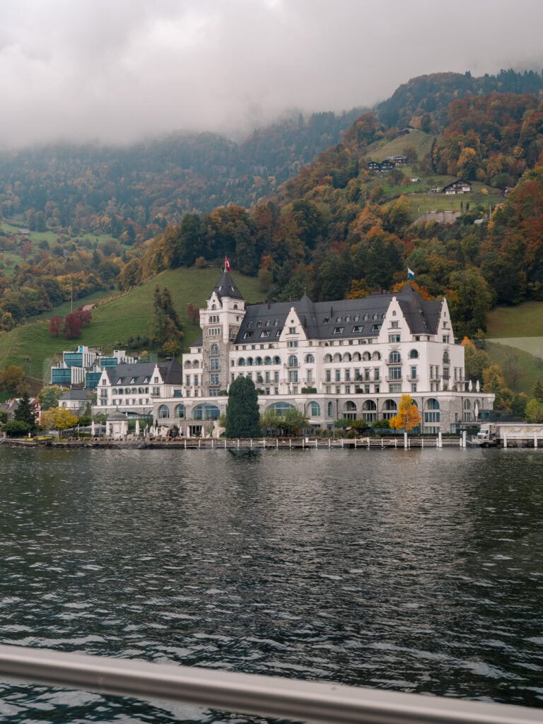 The grand Park Hotel Vitznau perched on the shore of Lake Lucerne with autumn trees behind it