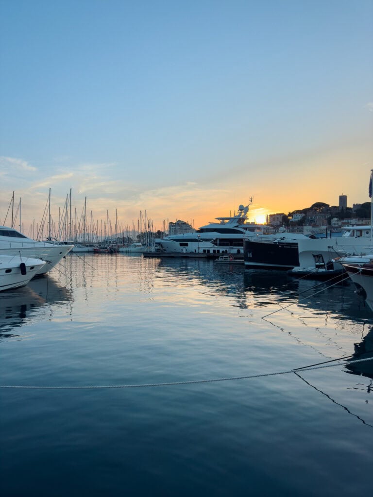 Yachts sit in Cannes harbour at sunset with reflections on calm water. The marina shows the glamorous side of a French Riviera public transport itinerary.