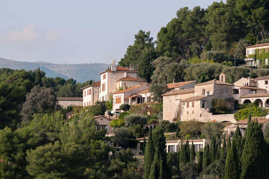 Stone houses and villas sit among trees on the hillside near Èze. The green slopes show the inland scenery beyond the coastal train line