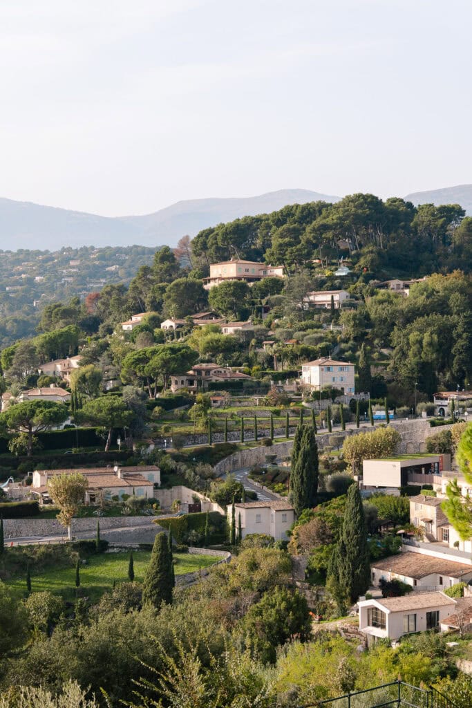 Hillside homes and villas sit among trees above Èze. The steep landscape explains why this village takes extra planning without a car