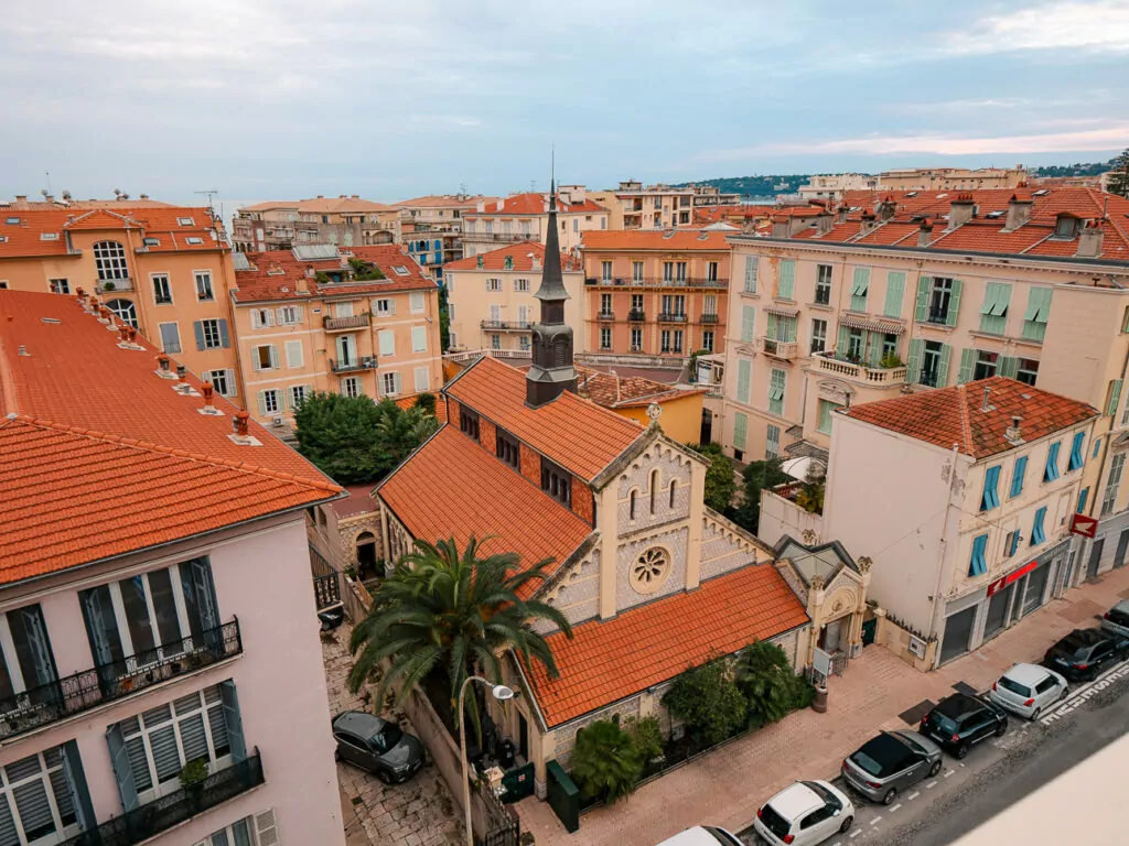 Menton rooftops and a small church are seen from above with terracotta tiles and pastel buildings. The sea sits just beyond the old town.