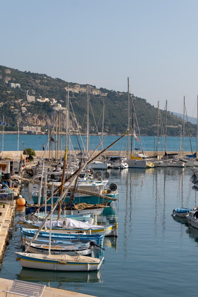 Sailboats and small fishing boats sit in Menton harbour with green hills behind them. The marina adds another easy waterfront stop to a car free Côte dAzur trip