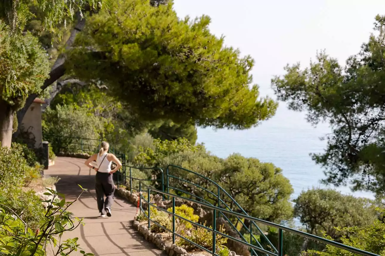 solo female traveller walking down a path in Monaco's gardens looking out to the water
