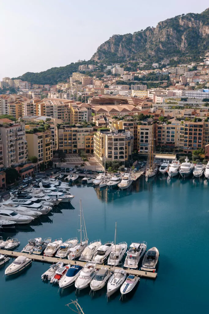 Monaco harbour seen from above with yachts packed into bright blue water. Hillside apartment blocks rise steeply behind Port Hercule.
