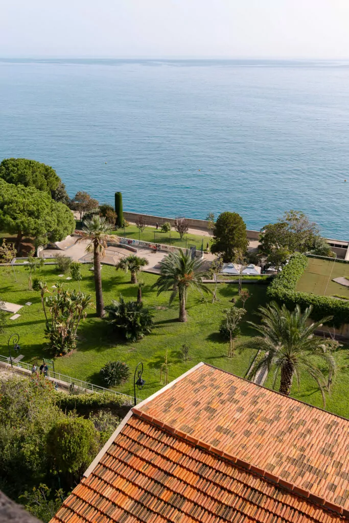 A terracotta roof and palm filled garden look out over the blue sea in Monaco. The high viewpoint shows the coastal side of the tiny country