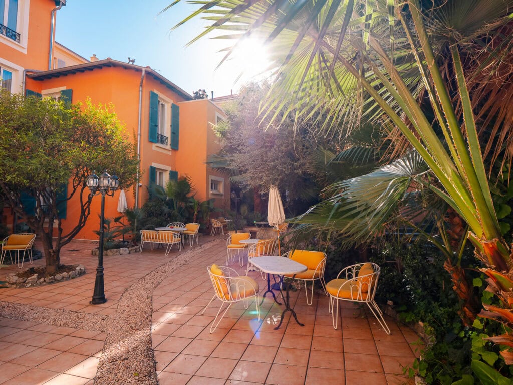 A sunny orange hotel courtyard in Nice with yellow chairs and palm trees. The bright patio shows a relaxing place to stay near public transport