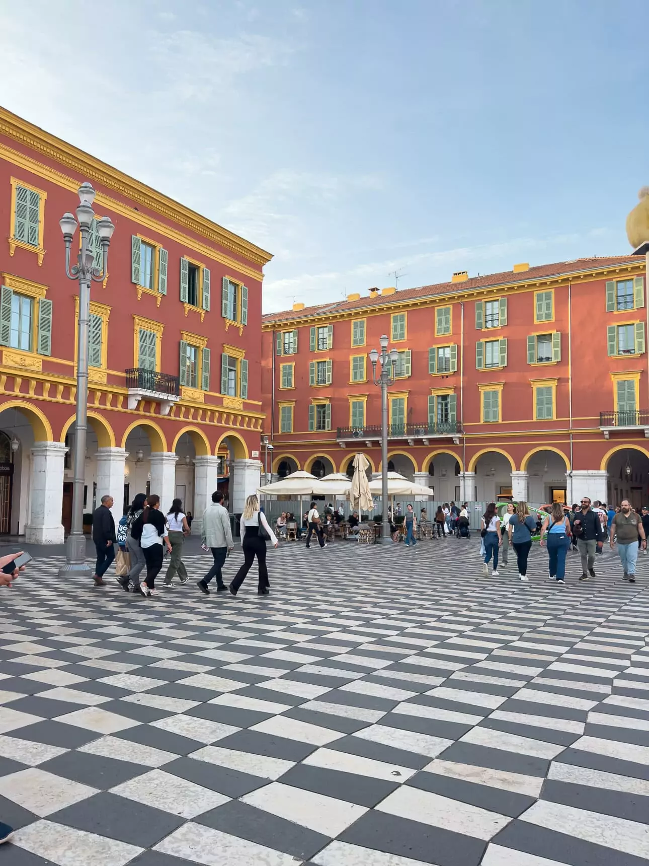 People walk across Place Masséna in Nice with red buildings and a black and white checkerboard square