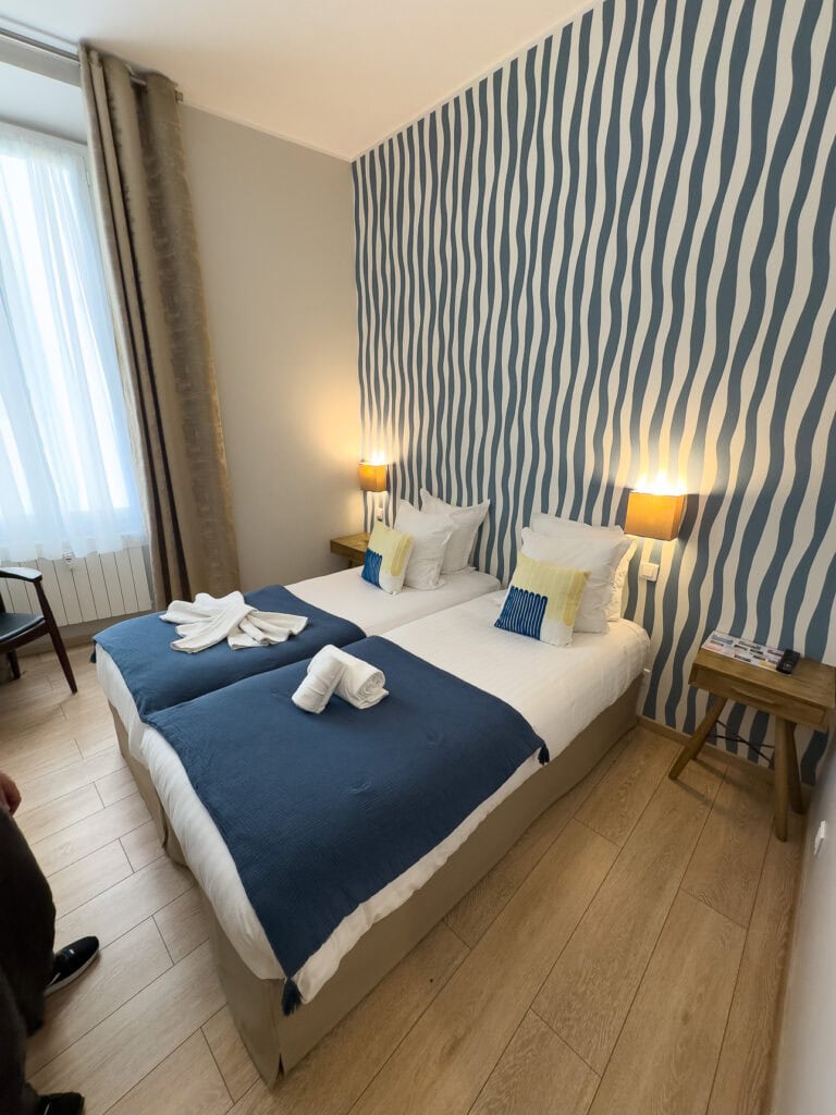 A simple twin hotel room in Nice with blue blankets and striped wallpaper. The room is a practical budget stay near the train station