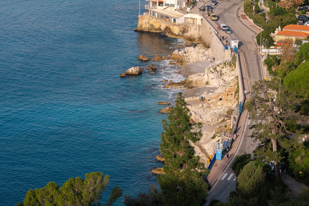 The Villefranche coastline seen from above with deep blue water and a road curving along the cliffs. This viewpoint shows the Riviera scenery between coastal train stops