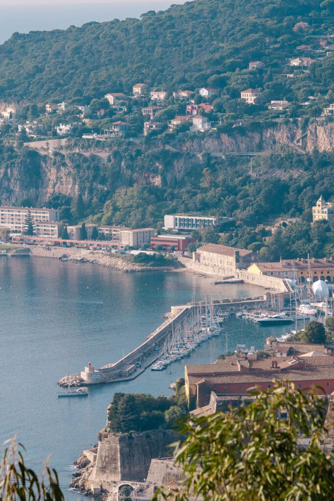 Villefranche harbour and hillside homes seen from a high viewpoint. Boats sit below the cliffs with the bay stretching behind them