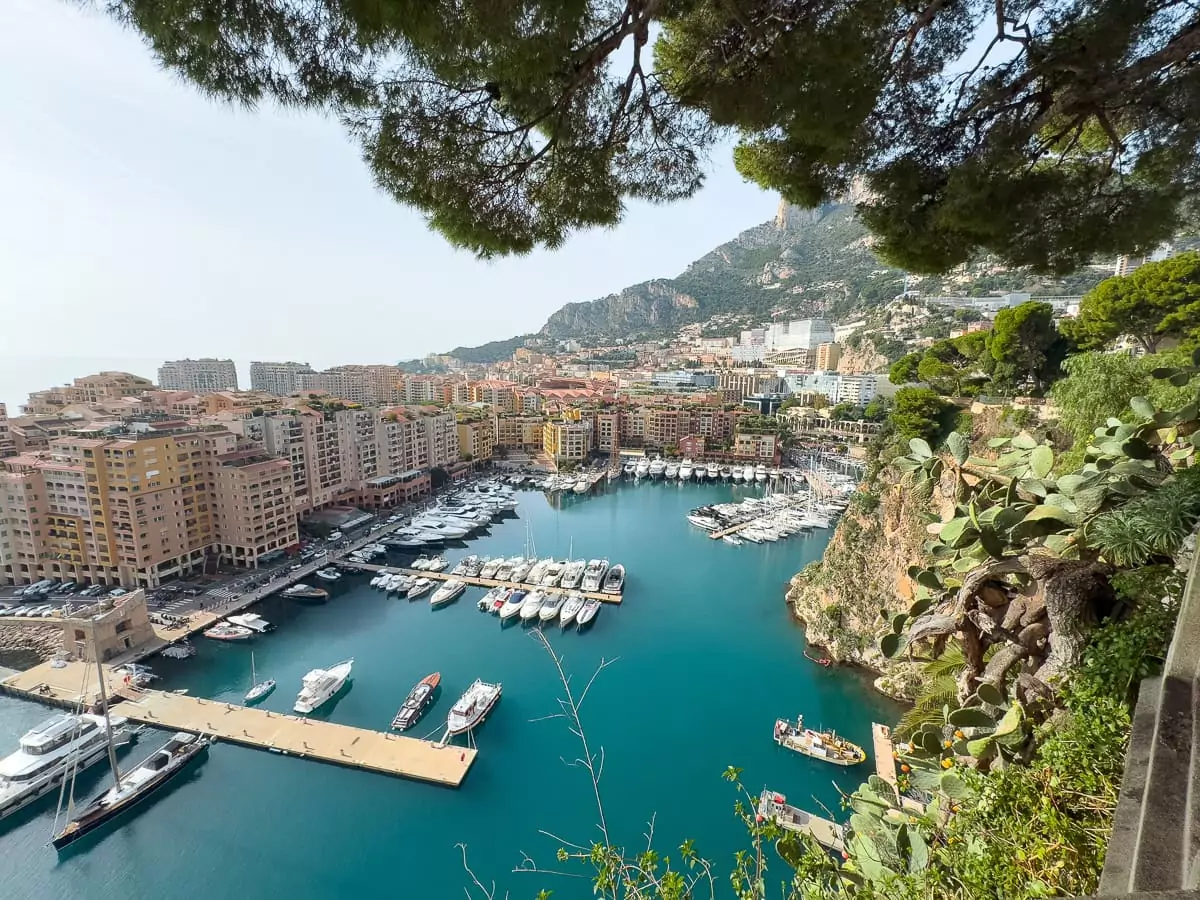Port Hercule in Monaco viewed from above with yachts in bright blue water. This harbour viewpoint is an easy coastal day trip when exploring the French Riviera by train
