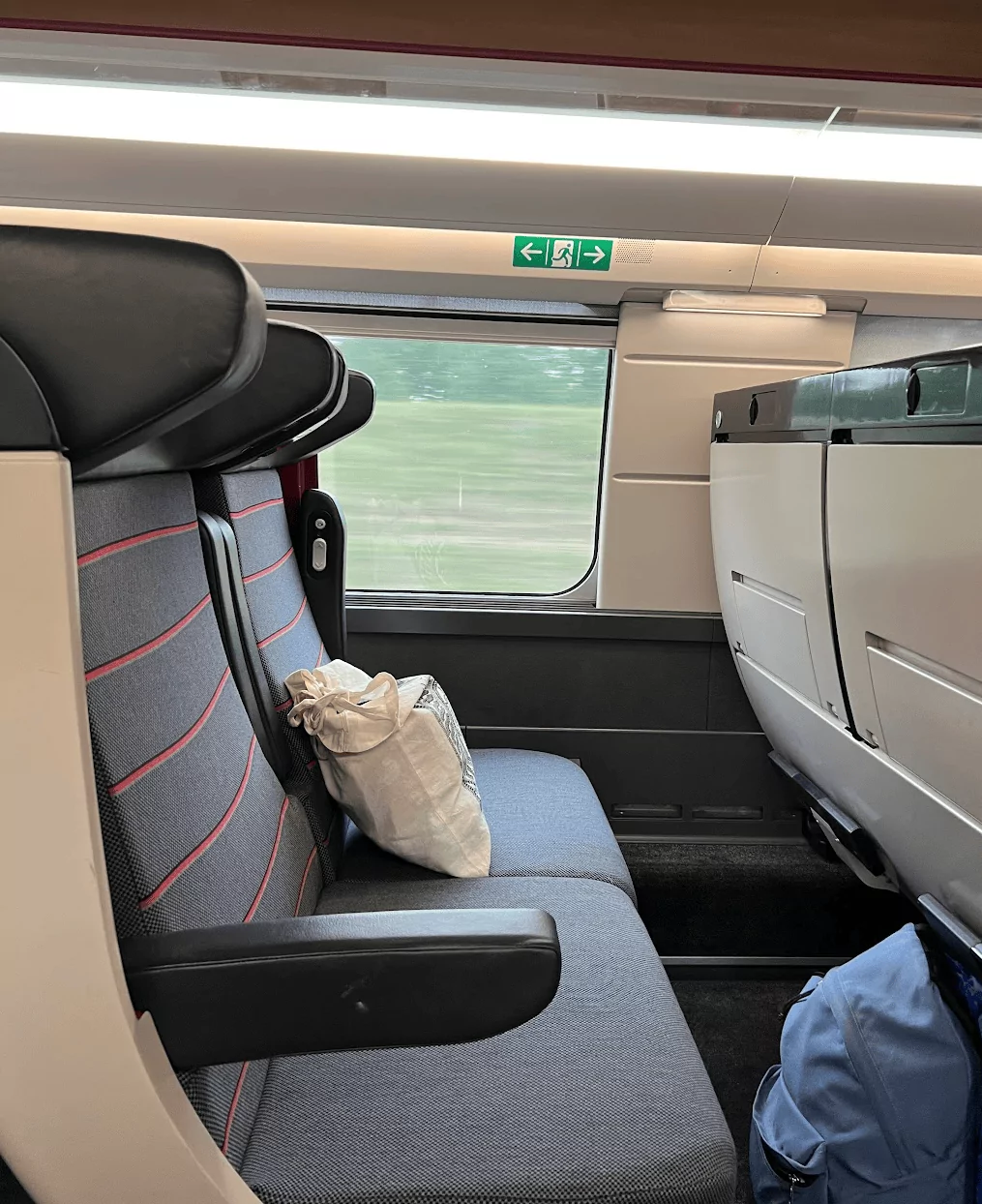 A train seat beside a window with bags on the seat and floor. This shows what a regional train journey can look like when travelling the French Riviera without a car