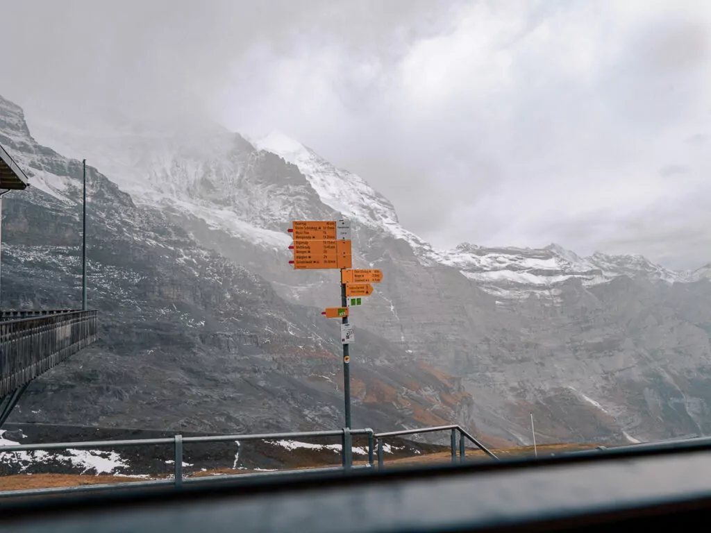 Hiking sign near Jungfraujoch with snowy mountains and clouds behind it