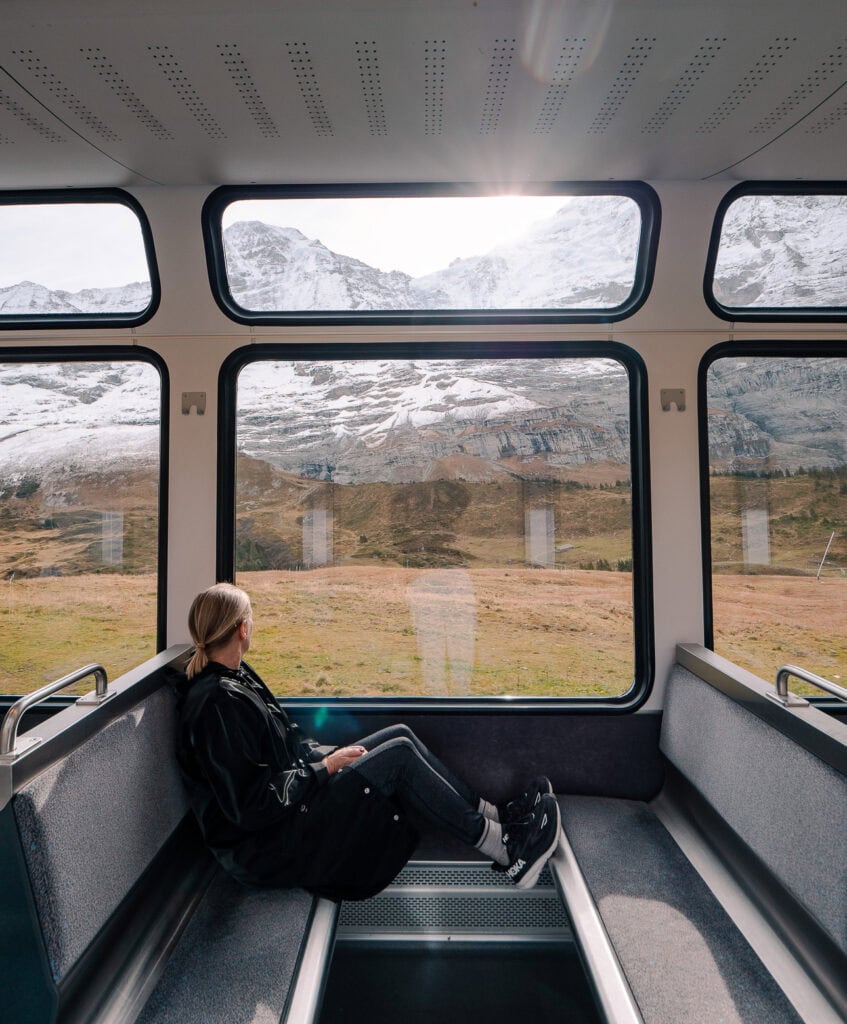 Traveller sitting inside a Swiss mountain train with snowy peaks visible through the panoramic windows