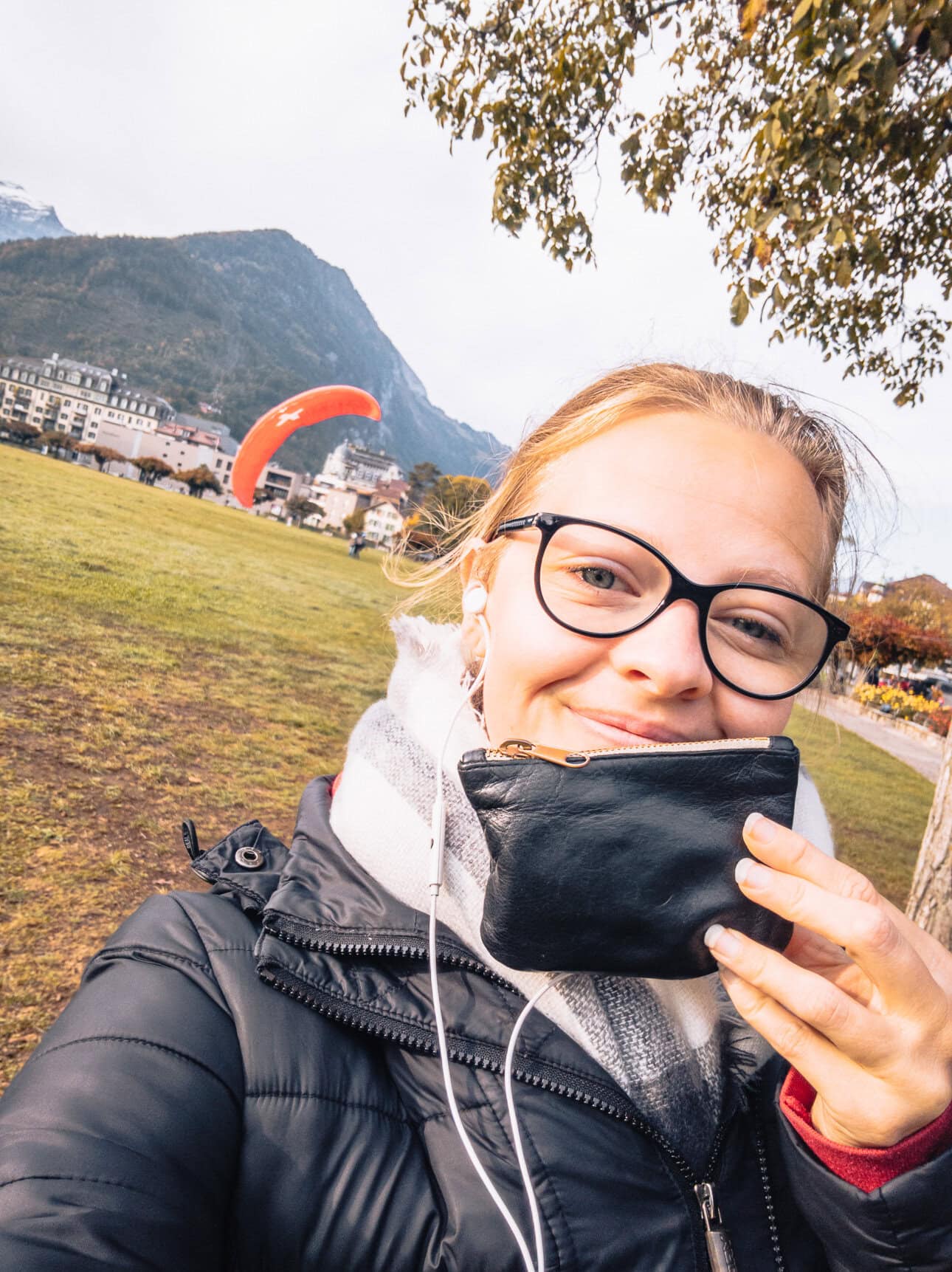 Alexx standing in front of a field where paragliders are landing behind her, holding her wallet in her hand after it was found by a bus driver