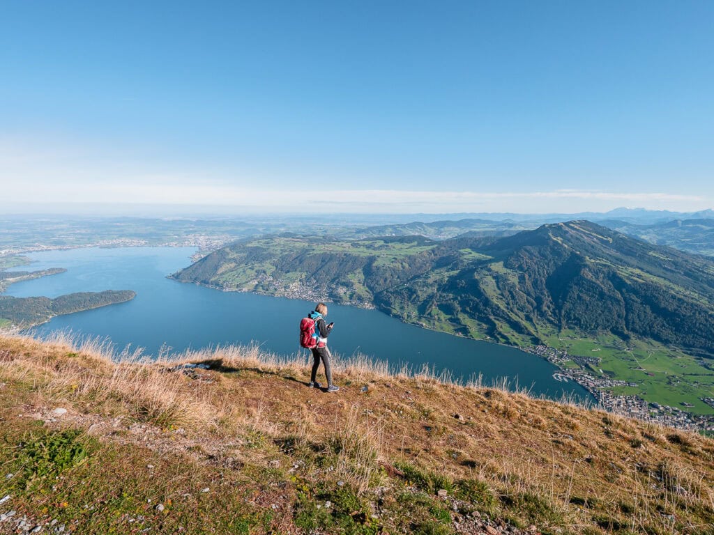 A hiker on a trail at the top of Mount Rigi with Lake Lucerne in the background. This is another of the few mountains fully included in various Switzerland travel passes.