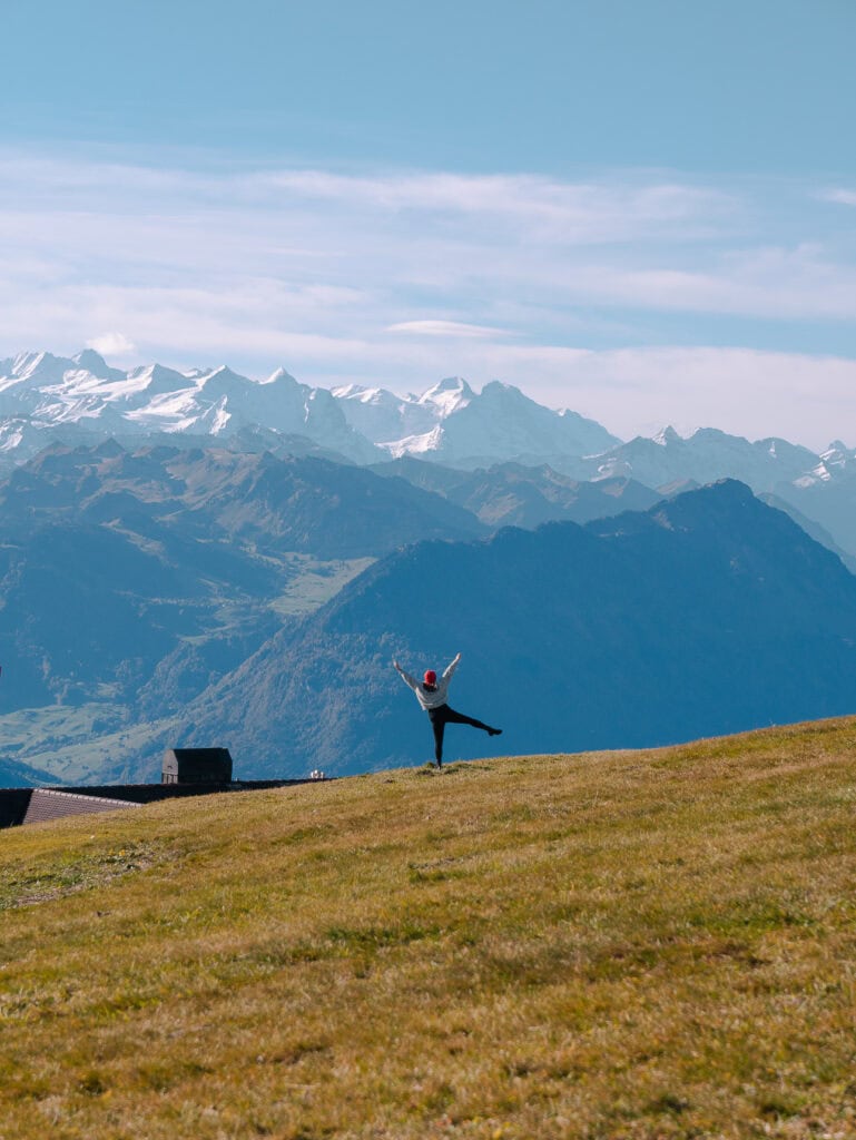 Traveller posing on a grassy hillside at the top of Mount Rigi with Swiss Alps mountain views in the background