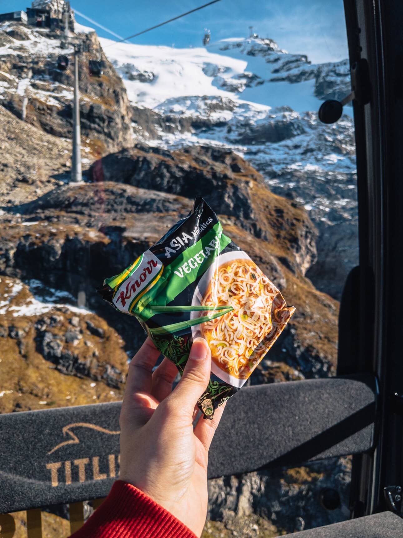 A traveller holds a packet of two minute noodles in their hand while catching the Titlis cable car, showing a way to save money in Switzerland