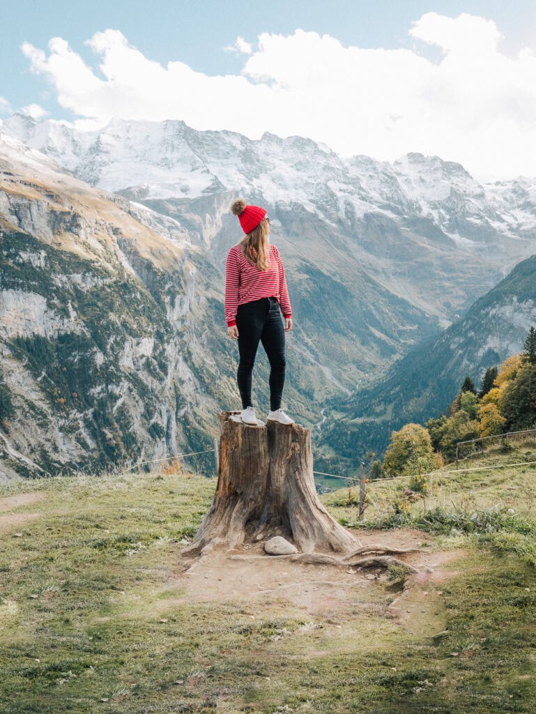 Alexx standing on a tree stump in front of snow covered mountain scenery near Murren in the Bernese Oberland