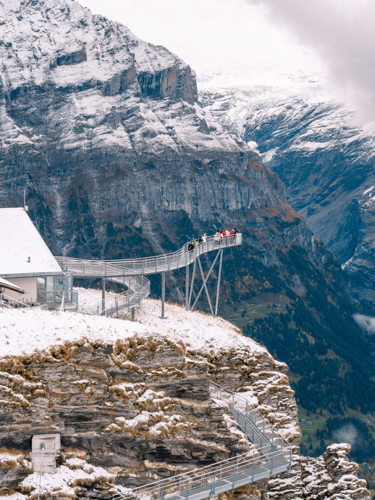 Grindelwald First cliff walk covered in snow, with a narrow metal walkway running along the rock face