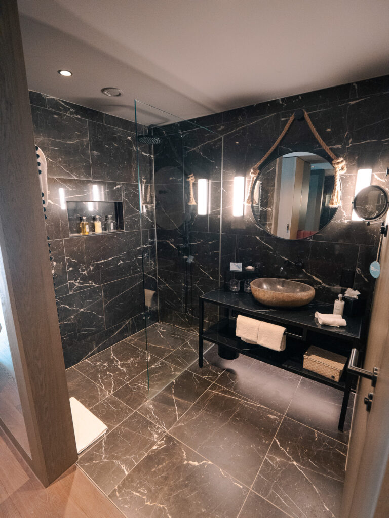 Bergwelt Grindelwald bathroom with twin circular mirrors, dark stone surfaces, and warm lighting