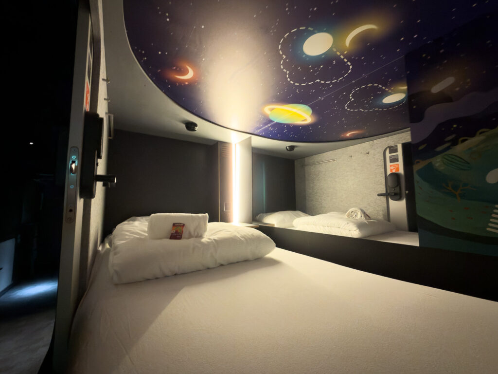 Capsule bed with white linen under a curved ceiling painted with planets and stars