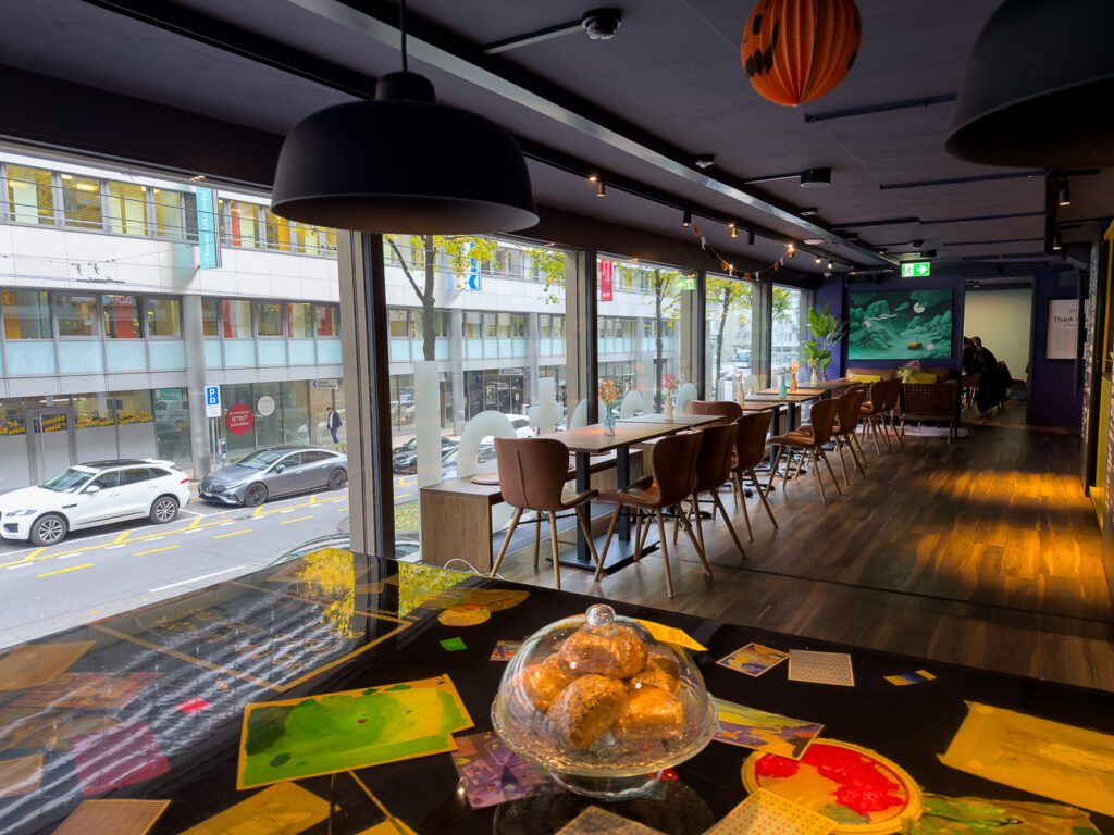 Communal tables, pendant lamps and pastries under a glass dome in a capsule hotel cafe