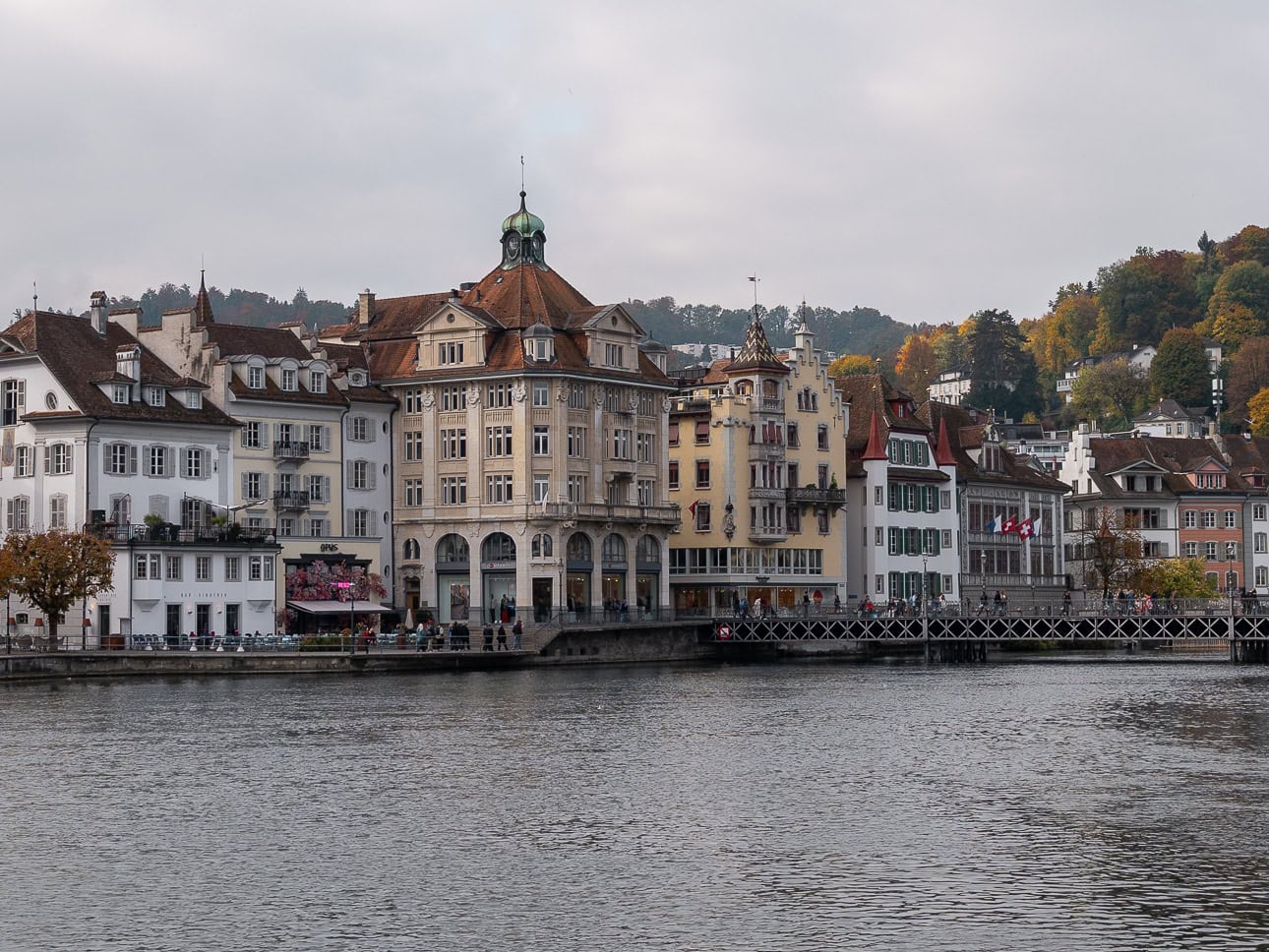 Riverside townhouses and a domed clock tower along the river Reuss in Lucerne under grey skies