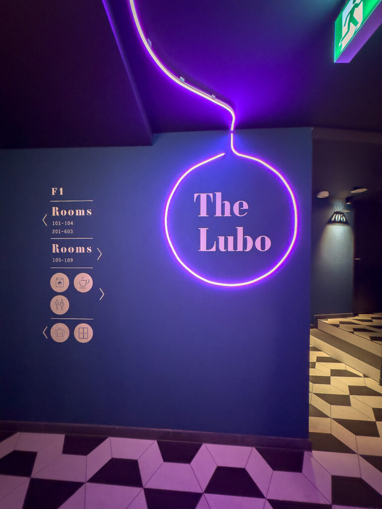 Neon circular sign reading The Lubo on a dark blue hotel corridor wall