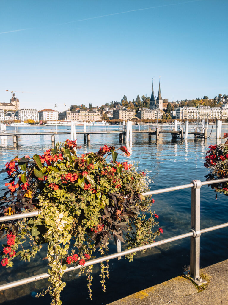 Lakeside promenade in Lucerne with red flower planters and the Hofkirche towers opposite