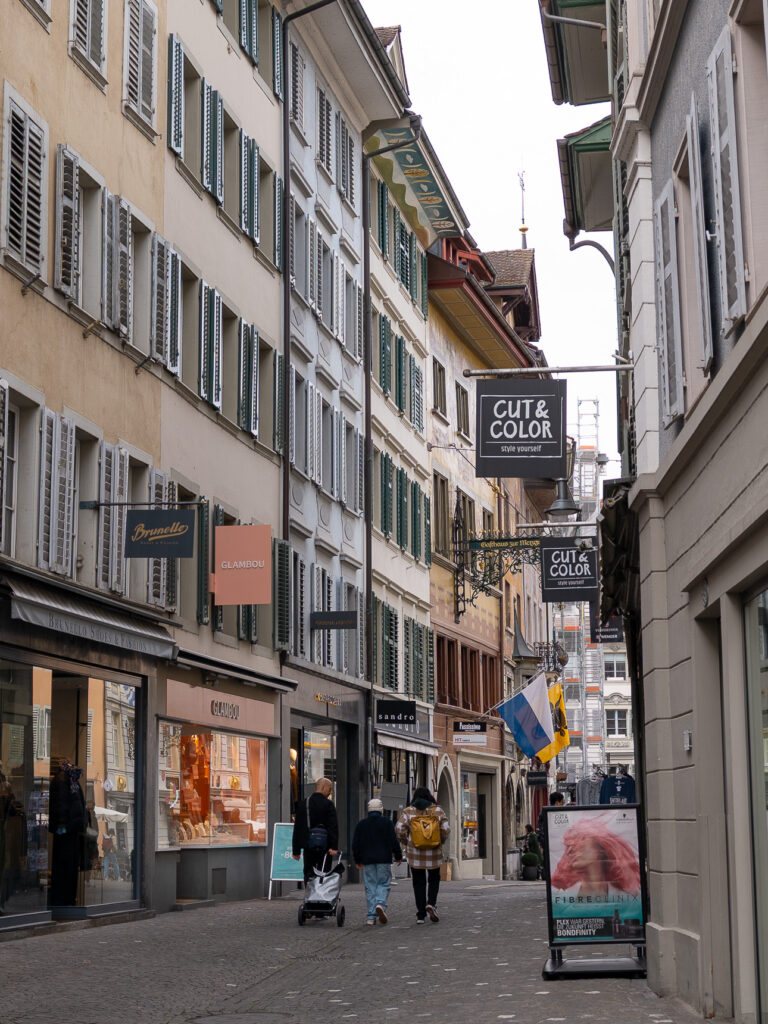Narrow cobbled shopping lane in Lucerne Old Town with hanging shop signs and people walking