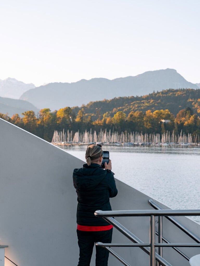 Traveller on a boat deck photographing a marina and autumn hills on Lake Lucerne
