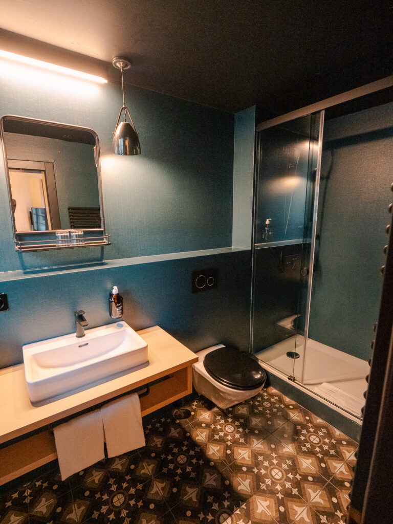 Hotel bathroom with teal walls, a white basin on a wooden shelf and a glass shower cubicle