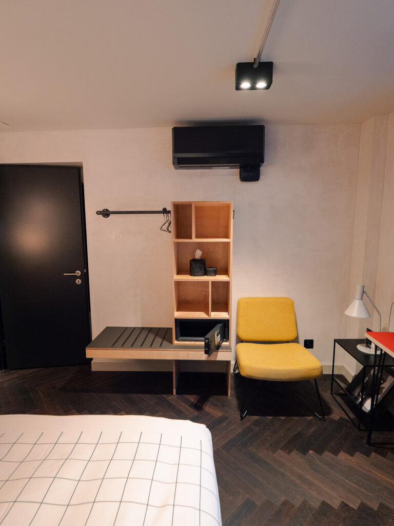 Room corner with an open hanging rail, shelving with a safe and a yellow armchair