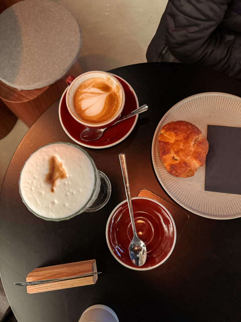Cafe table with a cappuccino, a foam-topped drink and a caramelised pastry, seen from above